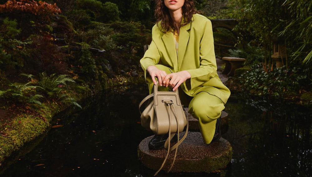 Coco wears a green toned suit and holds the Artichoke Dumpling Vegan Crossbody Bag in her hands