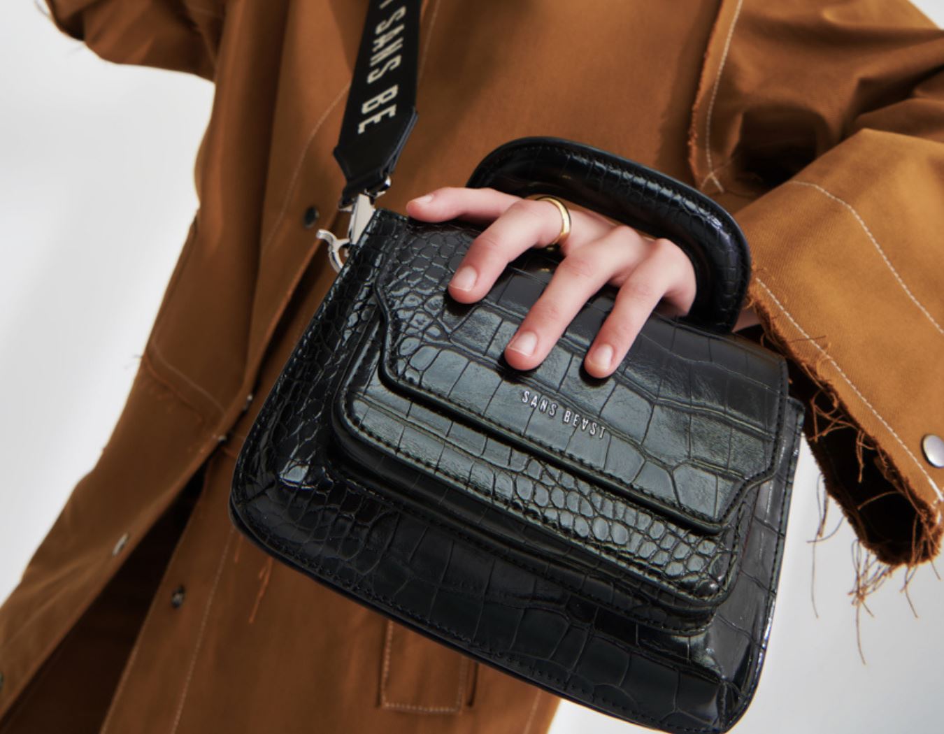 An closeup image of Paris holding a black Sans Beast Reader Satchel vegan handbag with faux croco finish.