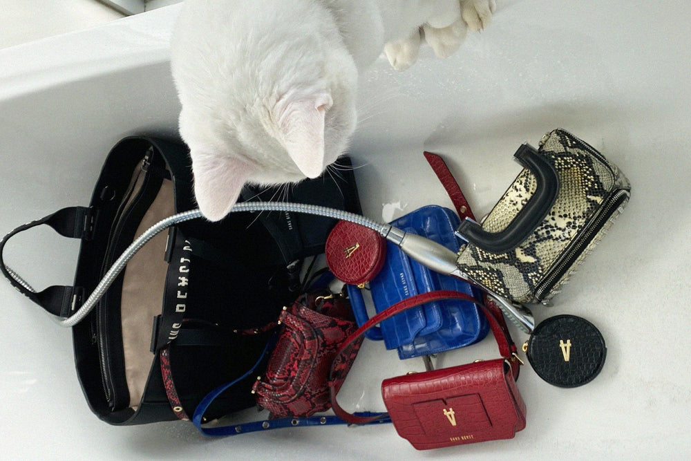 Luna the cat looks at a cluster of various Sans Beast vegan bags sitting in a white bathtub. 