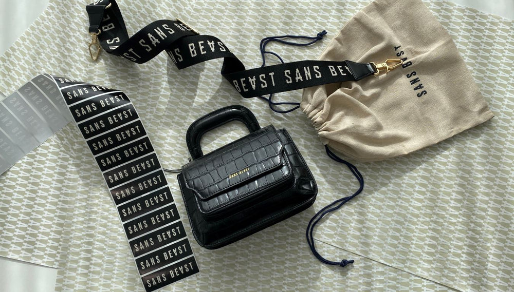 A flatlay image of a Sans Beast Reader Satchel + Barricade Strap with dustbag, printed tissue paper and stickers.