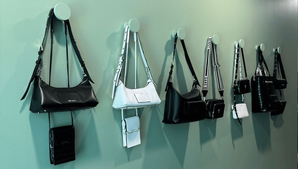 The green painted wall of the Sans Beast Studio, with various handbags in black + white hanging on oversized hooks.