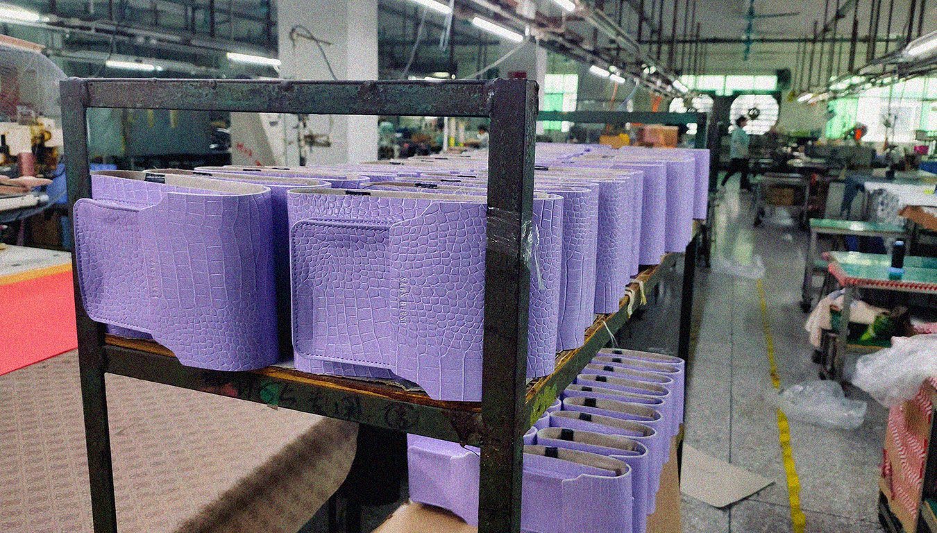 A group of purple toned Sans Beast vegan bags sit on shelving in a factory