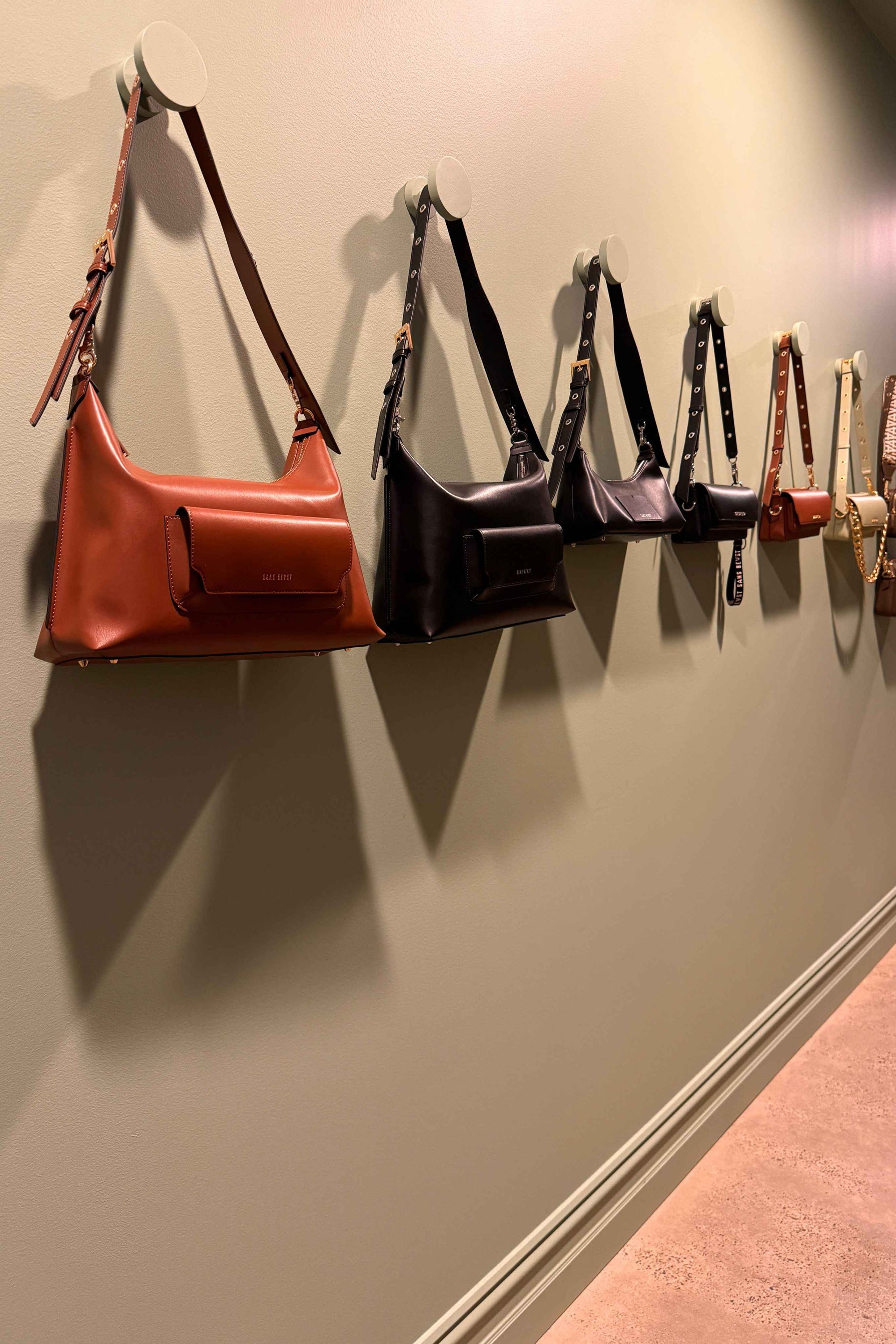 Vegan Handbags hang along a green wall in the Sans Beast Brunswick Studio in Melbourne, Australia